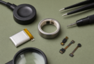 Macro photo of a smart ring repairability workbench with tiny battery, charging dock, and precision tools
