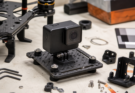 Unbranded action camera mounted on a vibration isolation plate beside drone and maker hardware