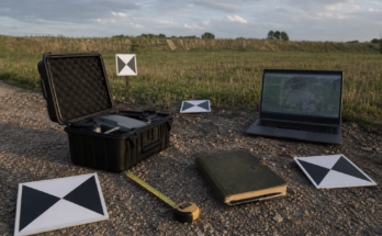 Outdoor field documentation setup with a small drone case, ground control targets, measuring tape, and laptop