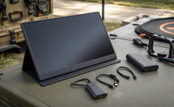 Portable monitor field kit with cables, battery, and camera gear on an outdoor work table