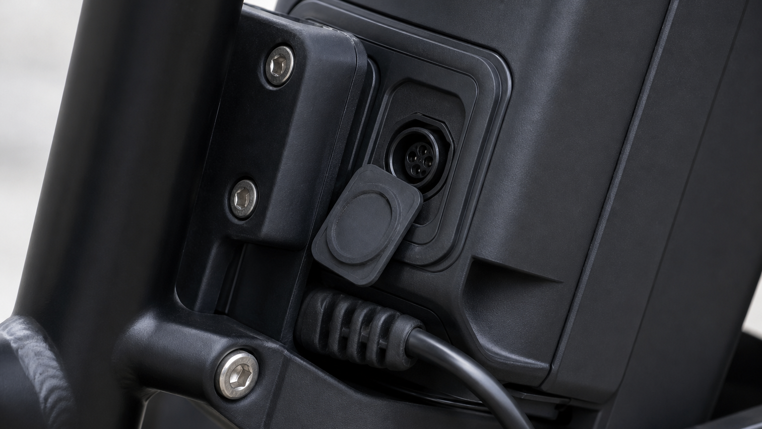 Close-up of an e-bike battery mount, weather seal, charge port cover, and cable strain relief, physically plausible hardware, neutral daylight, no tex