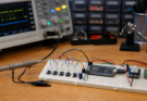 A pushbutton debouncing test bench with microcontroller, oscilloscope probe and tidy wiring.