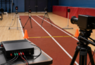 Timing gates, a camera tripod and a microcontroller data box arranged on an indoor track lane.