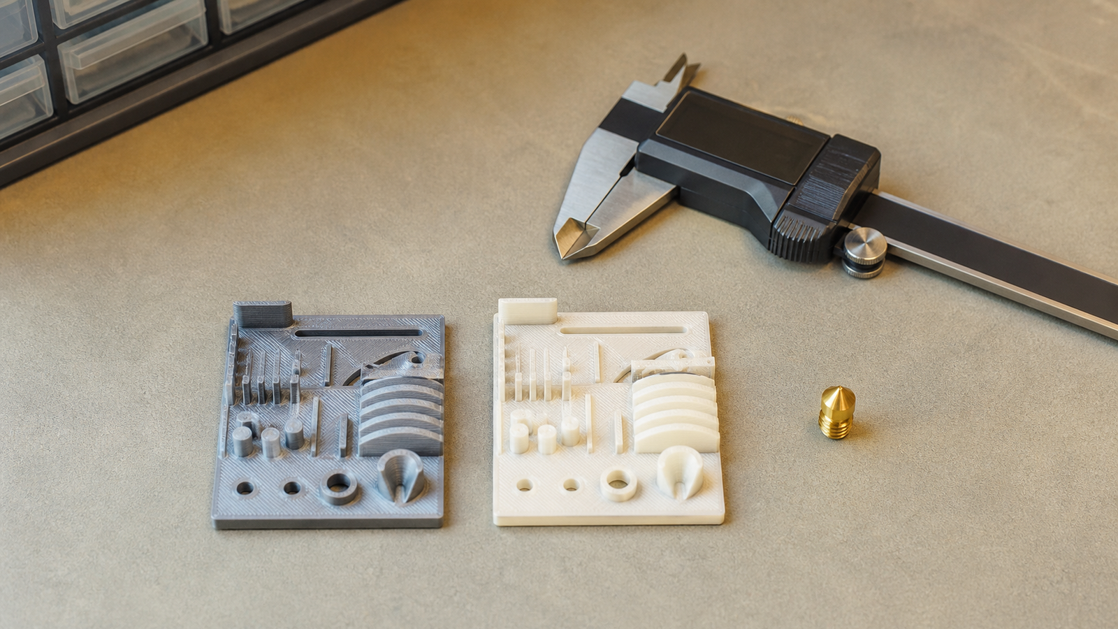 Two 3D-printed calibration coupons compared beside a clean spare nozzle and caliper