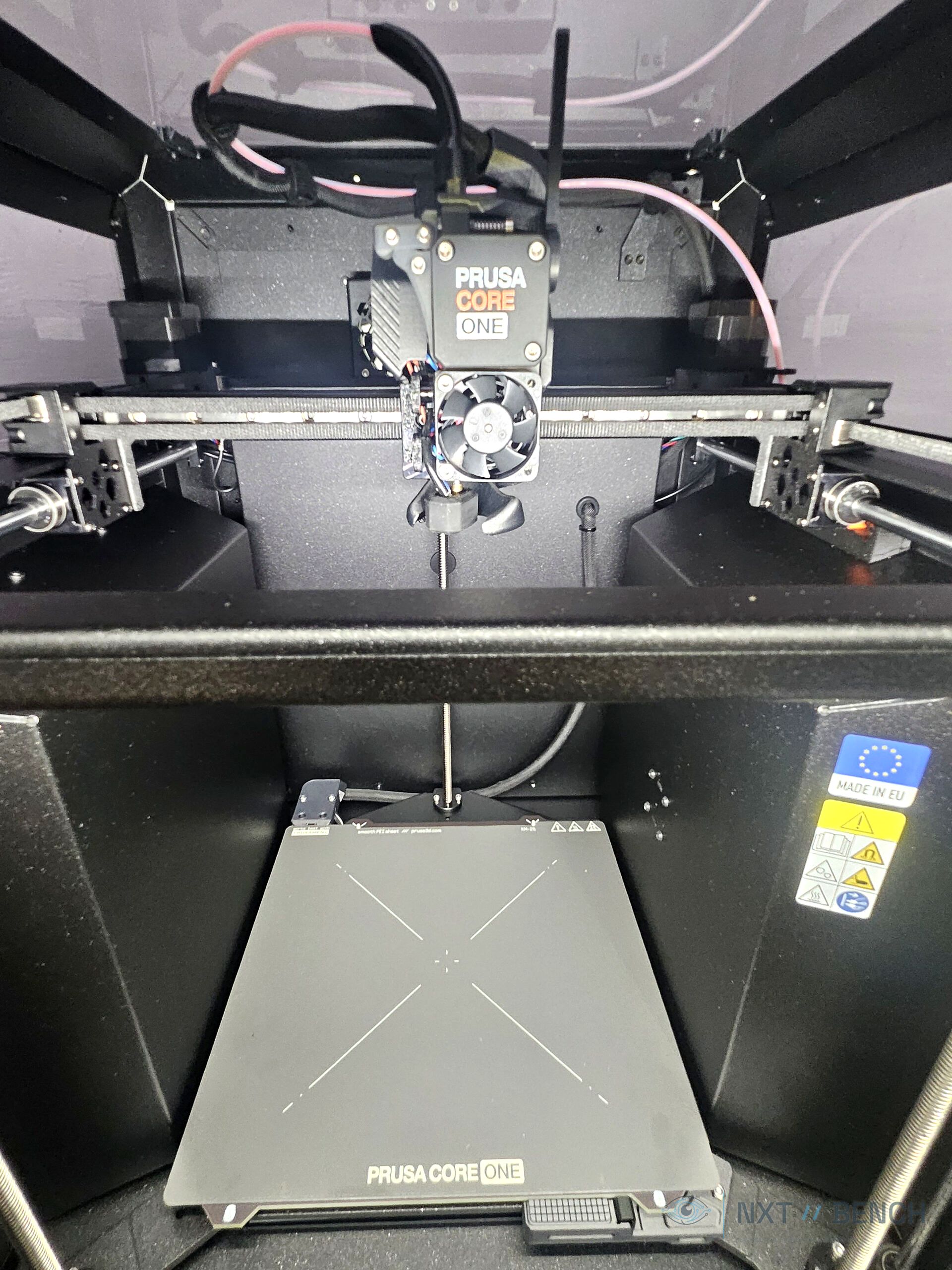 Close-up inside the Prusa CORE One+ showing visible 3D-printed components and blue interior lighting.