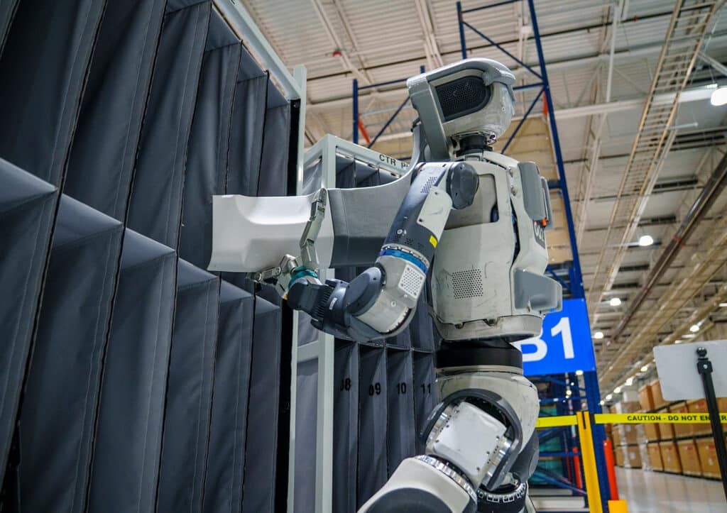 Boston Dynamics Atlas handling a component at an industrial workstation